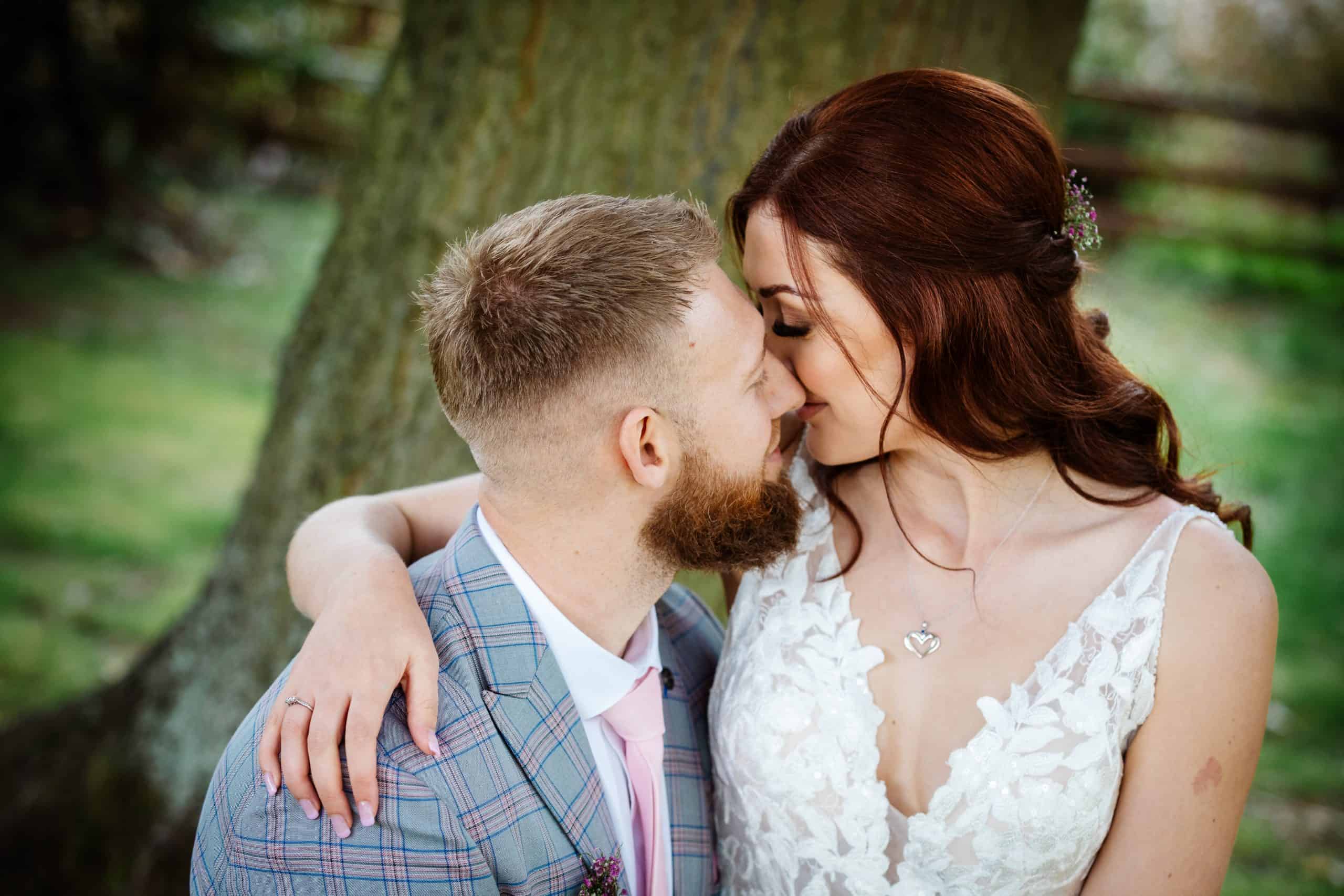A couple in wedding attire embrace outdoors, sitting close to each other with their faces nearly touching. Drawn by Light Photography